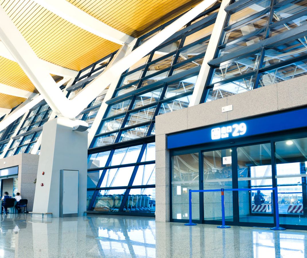 Ein großer Flughafen-Terminal mit zahlreichen Reisenden, Check-in-Schaltern und großen Fenstern, die auf das Rollfeld blicken.