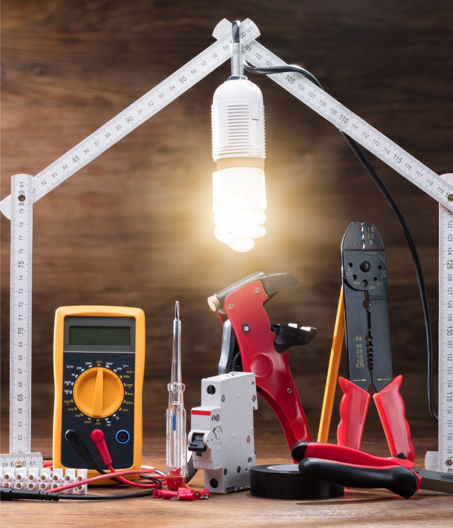 Auf einem Holztisch liegen elektrische Werkzeuge und eine Glühbirne, die für handwerkliche Arbeiten verwendet werden können.